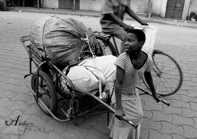 A burden bearer pulls a heavy cart down the street.
