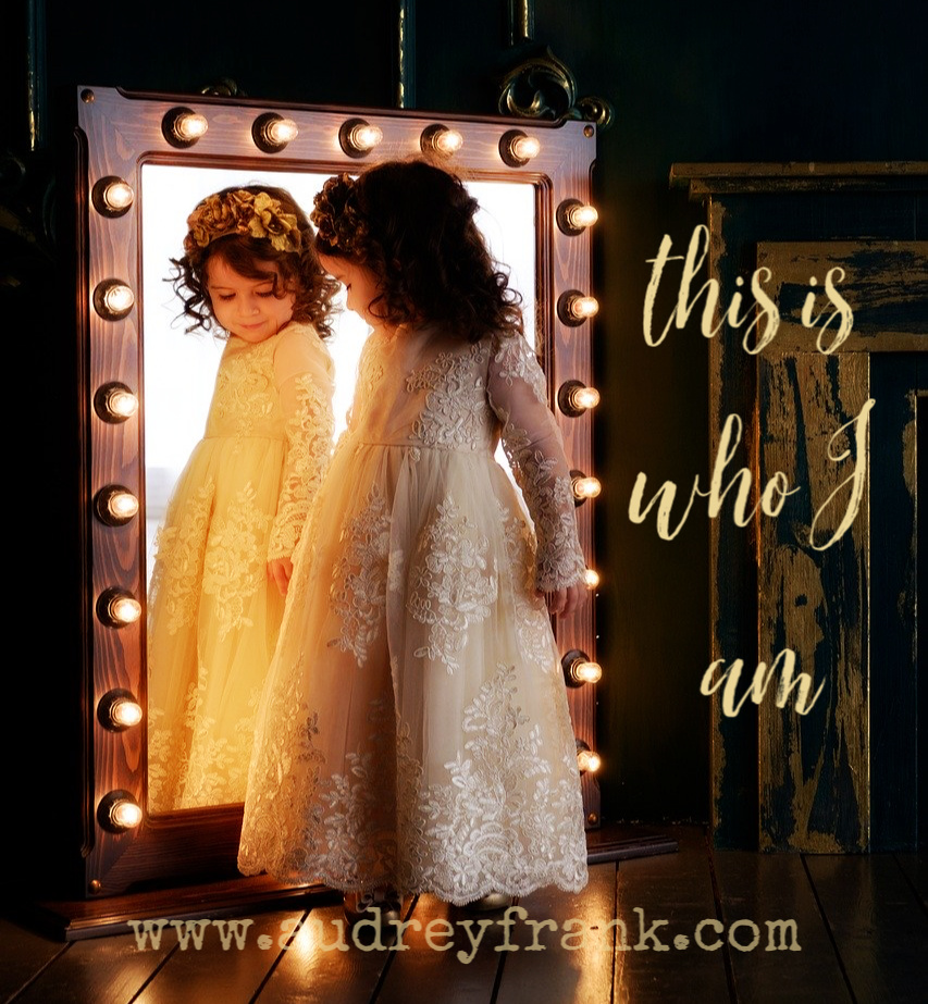 A little girl dressed in a princess dress looks at herself in a mirror. The words "This is who I am" describe the subject of the article.
