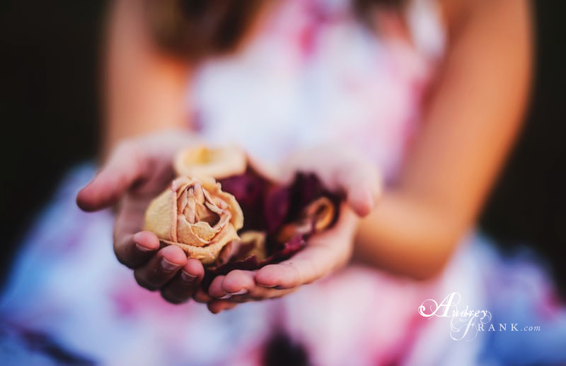 Girl holding dried roses in outstretched hand, entrusting her gift to the receiver.