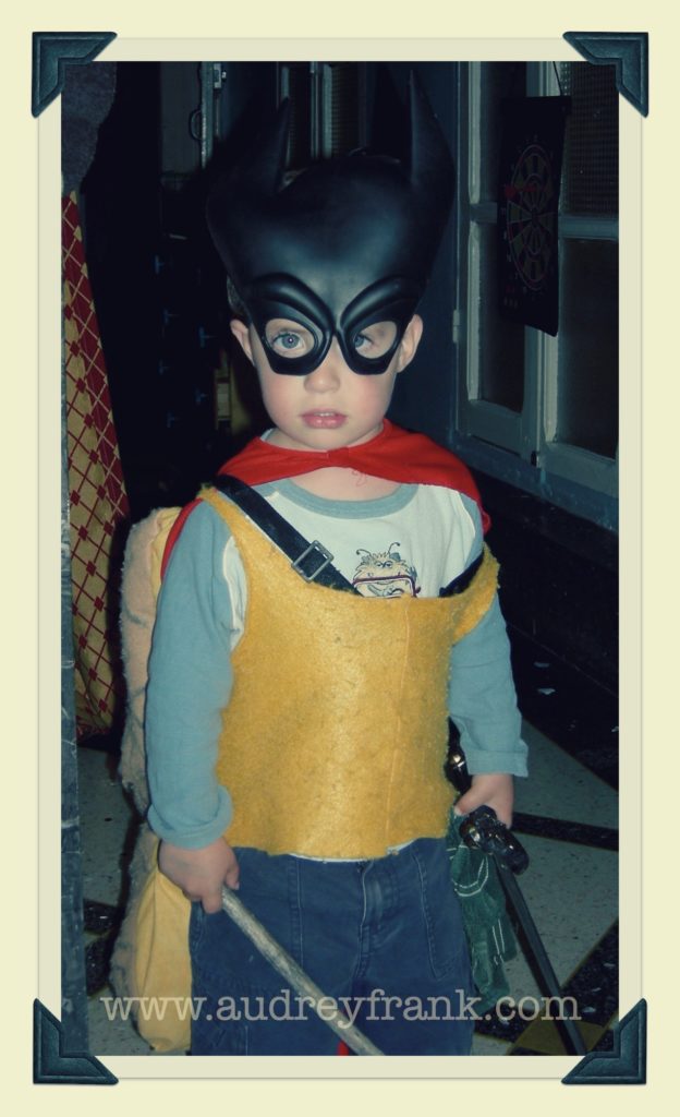 a little boy in a super hero costume carrying a stick and a sword