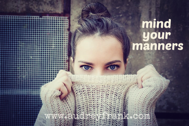 a girl peeking over the neck of her sweater with the words "mind your manners"