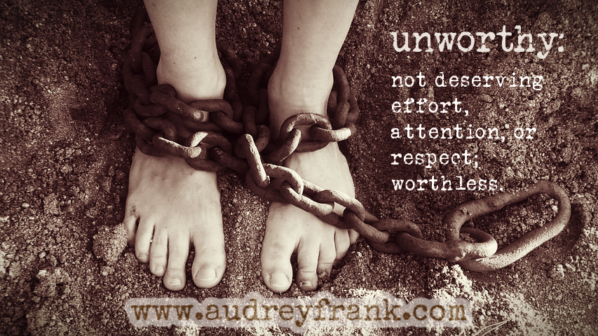 Bare feet bound in chains. The words "unworthy: not deserving effort, attention, or respect; worthless."