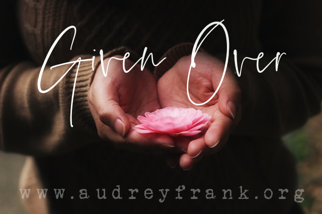 Hands holding a pink flower out as a gift with the words Given Over.
